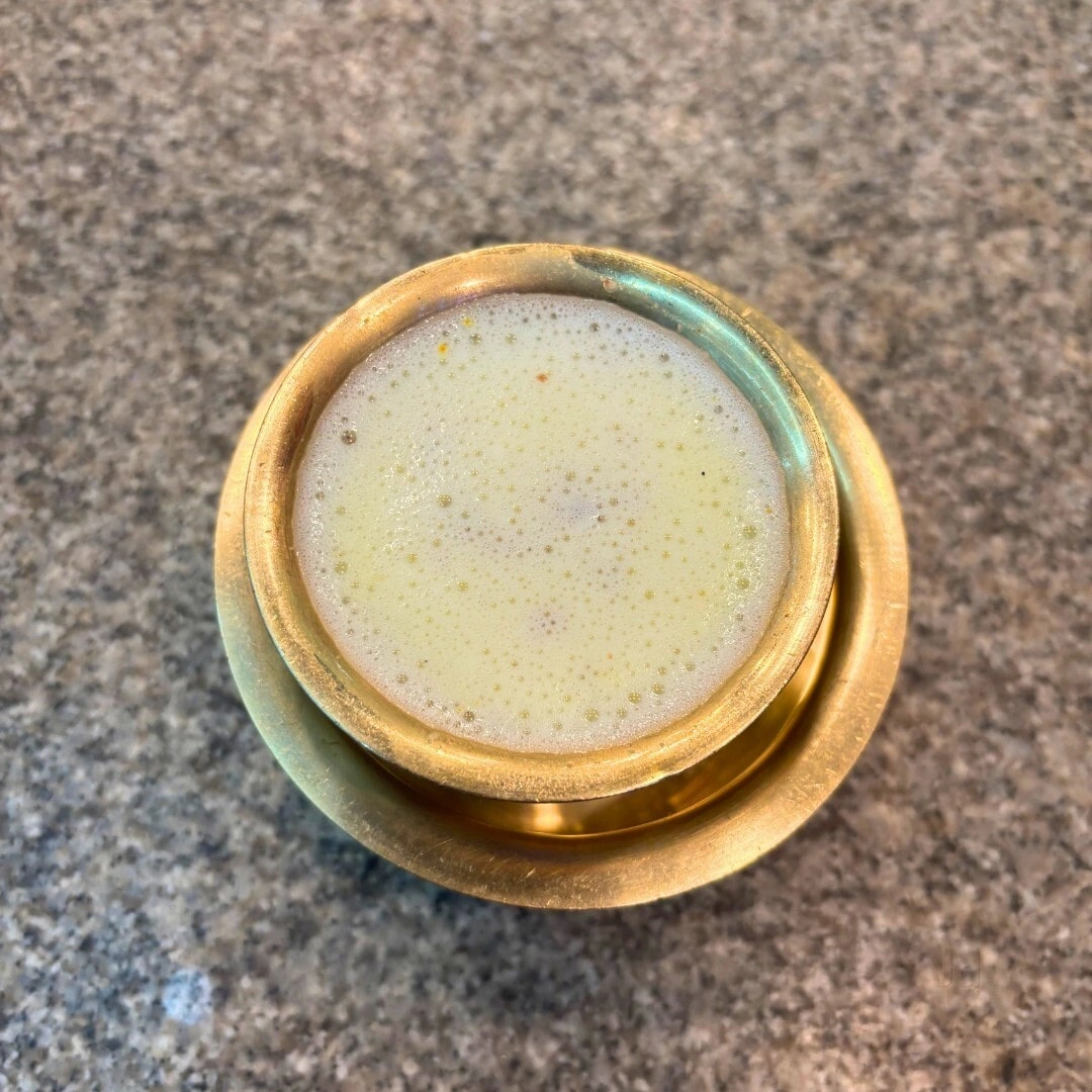 A warm drink presented in a brass cup and saucer