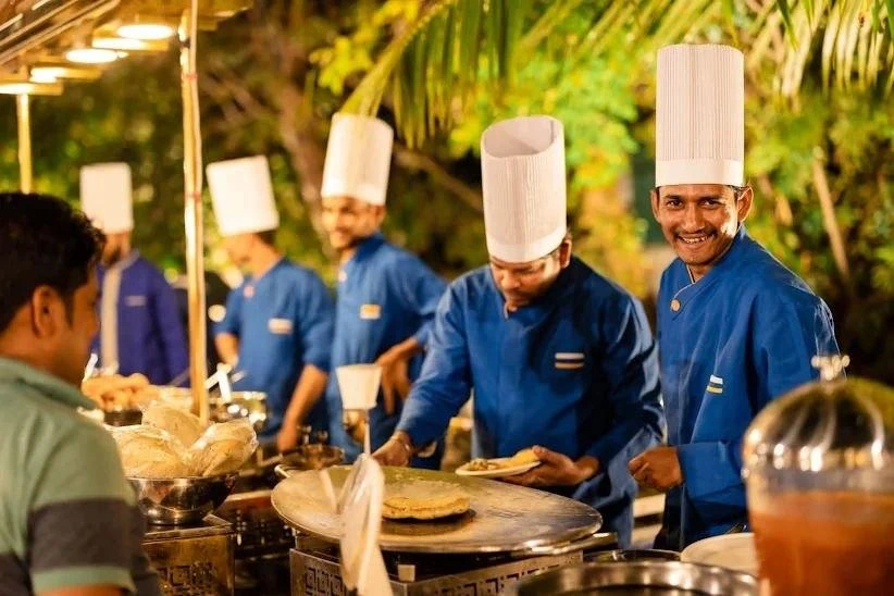 Chefs in blue uniforms preparing fresh dosa at a live catering counter