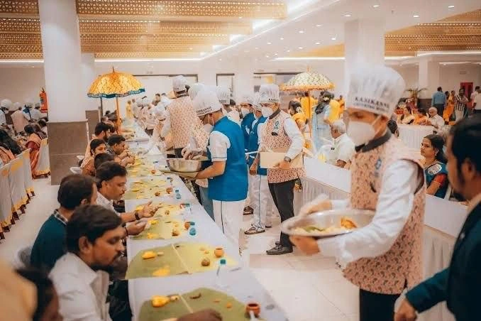 A catering team serving guests seated at a banana-leaf dining table